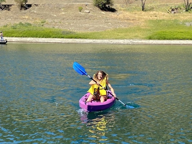 Woman kayaking in purple kayak on lake.